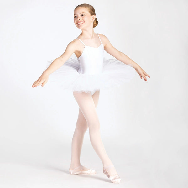 A young girl dancer posing in a white ballet leotard with a matching tutu skirt, light pink tights, and pointe shoes against a seamless white studio background.