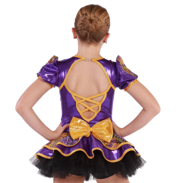 A child model shown from the back wearing a shiny purple dance costume with gold trim, a large gold bow at the back, and a black tutu skirt, against a plain white background.