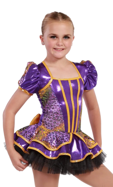 A young girl modeling a purple and gold sequined ballroom dance costume with a black tutu skirt, set against a plain white studio background.